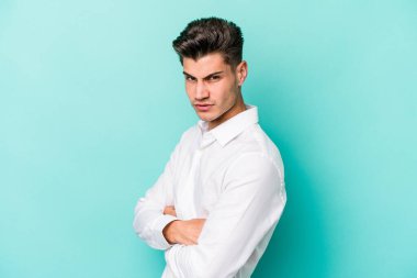 Kafkasyalı genç adam mavi arka planda izole edilmiş hoşnutsuzca kaşlarını çatmış, kollarını kavuşturmuş..