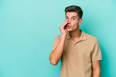 Mavi arka planda izole edilmiş genç beyaz bir adam gizli bir sıcak fren haberi veriyor ve yana bakıyor.