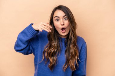 Beyazlı genç bir kadın bej arka planda izole edilmiş bir şekilde bir şeye gülüyor, ağızlarını elleriyle kapatıyor..