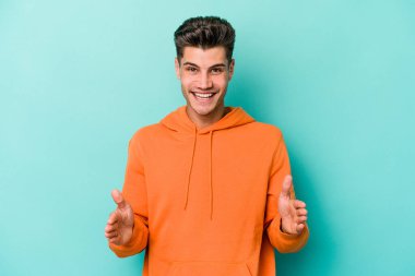 Mavi arka planda izole genç beyaz adam iki eliyle bir şey tutuyor, ürün sunumu..
