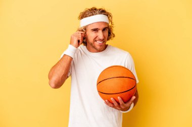 Young basketball player caucasian man isolated on yellow background covering ears with hands.