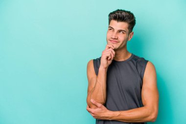 Mavi arka planda izole edilmiş genç beyaz adam rahatlamış bir şeyin fotokopi odasına baktığını düşünüyor..