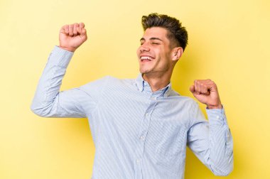 Sarı arka planda izole edilmiş genç beyaz adam özel bir günü kutluyor, atlıyor ve enerjiyle kollarını kaldırıyor..