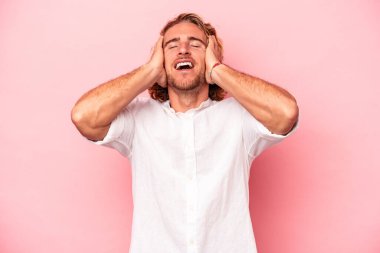 Pembe arka planda izole edilmiş genç beyaz adam ellerini başının üstünde tutarak neşeyle gülüyor. Mutluluk kavramı.