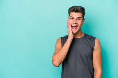 Mavi arka planda izole edilmiş genç beyaz adam yüksek sesle bağırıyor, gözleri açık ve elleri gergin tutuyor..