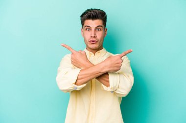 Mavi arka plan noktalarında izole genç beyaz adam, iki seçenek arasında seçim yapmaya çalışıyor.
