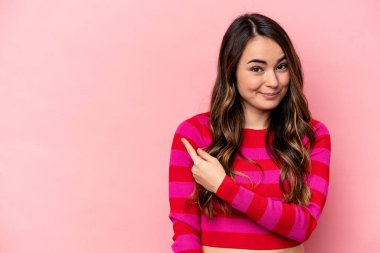 Pembe arka planda izole edilmiş genç beyaz kadın gülümsüyor ve boş alanda bir şeyler gösteriyor..