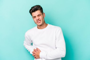 Mavi arka planda karaciğer ağrısı çeken, karnı ağrıyan genç beyaz bir adam..