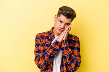 Sarı arka planda izole edilmiş genç beyaz adam esniyor. Ağzı eliyle kapatan yorgun bir hareket sergiliyor..