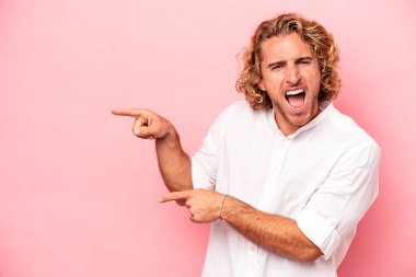 Pembe arka planda izole edilmiş genç beyaz adam işaret parmağıyla işaret ederek heyecanlanıyor..