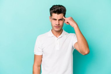 Mavi arka planda izole edilmiş genç beyaz bir adam şakağı parmağıyla işaret ediyor, düşünüyor ve bir göreve odaklanıyor..