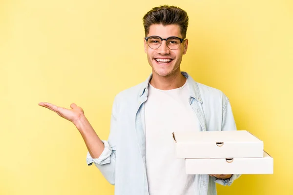 Mladý Kavkazský Muž Drží Pizzy Izolované Žlutém Pozadí Ukazující Kopírovací — Stock fotografie