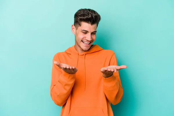 Jovem Caucasiano Isolado Fundo Azul Segurando Algo Com Palmas Das — Fotografia de Stock