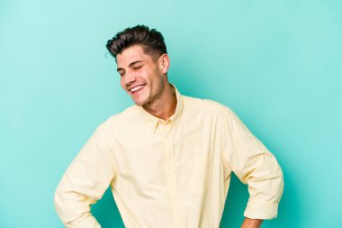 Kafkasyalı genç, mavi arka planda izole edilmiş. Kendine güvenen, kalçaları tutan biri..