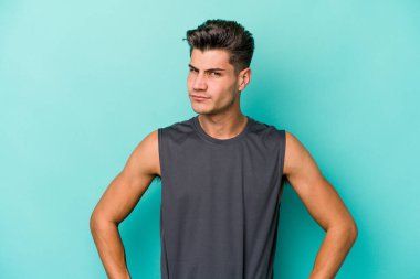 Kafkasyalı genç adam mavi arka planda izole edilmiş hoşnutsuzca kaşlarını çatmış, kollarını kavuşturmuş..