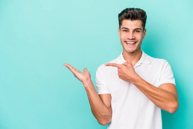 Kafkasyalı genç adam mavi arka planda izole edilmiş. Elinde palmiye ağacının bir kopyası olduğu için heyecanlı..