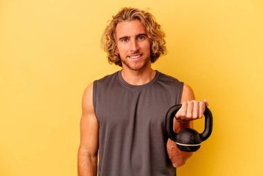 young sport man making weightlifting isolated on yellow background happy, smiling and cheerful.