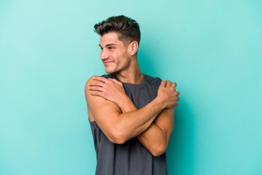 Kafkasyalı genç adam mavi arka planda izole edilmiş, güler yüzlü ve mutlu..