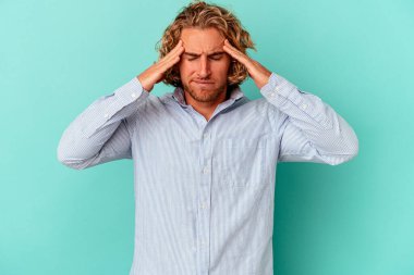 Genç beyaz adam mavi arka planda izole edilmiş tapınaklara dokunuyor ve başı ağrıyor..