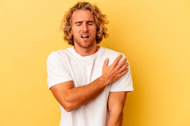 Sarı arka planda izole edilmiş, omuz ağrısı olan genç beyaz bir adam..