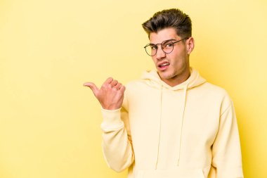 Sarı arka planda izole edilmiş genç beyaz adam işaret parmağıyla fotokopi alanını işaret ederek şok oldu..