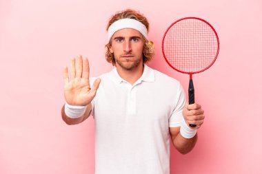 Badminton oynayan beyaz bir genç, pembe arka planda izole edilmiş, elini uzatmış, dur işaretini göstererek seni engelliyor..