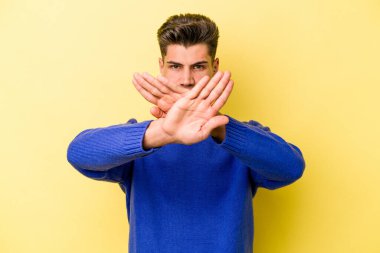 Sarı arka planda izole edilmiş genç beyaz adam inkar jesti yapıyor.