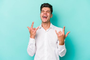 Mavi arka planda izole edilmiş genç beyaz adam boynuzlarını devrim konsepti olarak gösteriyor..