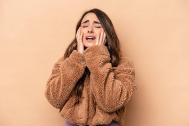 Beyaz tenli genç bir kadın bej arka planda izole edilmiş sızlanıyor ve ağlıyordu..