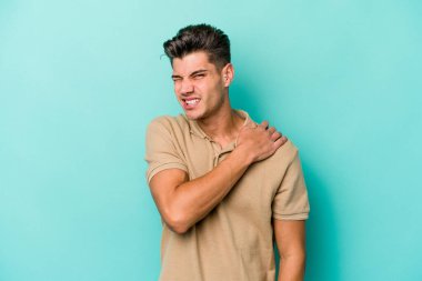 Mavi arka planda izole edilmiş, omuz ağrısı olan genç beyaz bir adam..