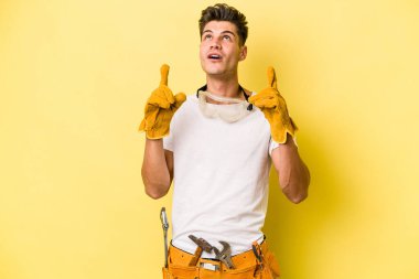 Young electrician caucasian man isolated on yellow background pointing upside with opened mouth.