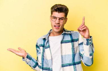 Genç beyaz adam sarı arka planda izole edilmiş ve elinde bir ürün var..