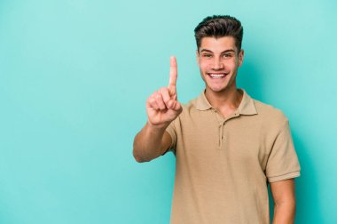 Mavi arka planda izole edilmiş genç beyaz adam bir numarayı parmağıyla gösteriyor..