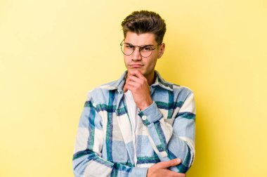 Kafkasyalı genç adam sarı arka planda izole edilmiş düşünüyor ve yukarı bakıyor, yansıtıyor, düşünüyor, hayal kuruyor..