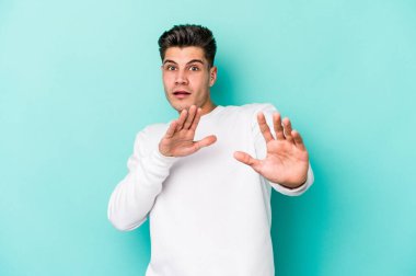 Mavi arka planda izole genç beyaz adam yakın bir tehlike nedeniyle şoka uğruyor