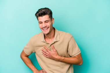 Kafkasyalı genç adam mavi arka planda izole olmuş gülüyor, elini yüreğine koyuyor, mutluluk kavramını koruyor..