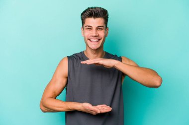 Mavi arka planda izole genç beyaz adam iki eliyle bir şey tutuyor, ürün sunumu..