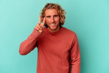 Mavi arka planda izole edilmiş genç beyaz adam iki numarayı parmaklarıyla gösteriyor..