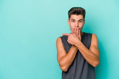 Mavi arka planda izole edilmiş genç beyaz adam yan tarafı işaret ediyor.