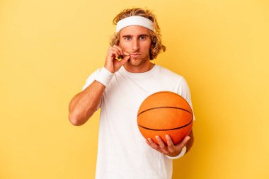 Young basketball player caucasian man isolated on yellow background with fingers on lips keeping a secret.