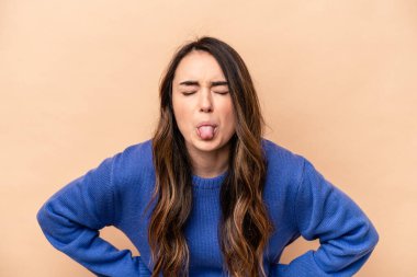 Beyaz tenli genç bir kadın bej arka planda izole edilmiş komik ve dost canlısı bir dil kullanıyor..