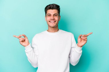Mavi arka planda izole edilmiş genç beyaz adam farklı kopya alanlarını gösteriyor, birini seçiyor, parmaklarıyla gösteriyor.