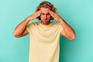Kafkasyalı genç bir adam mavi arka planda izole edilmiş, başı ağrıyor, yüzüne dokunuyor..
