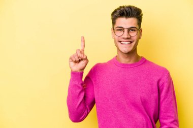 Sarı arka planda izole genç beyaz adam parmak ile bir numara gösteriyor.