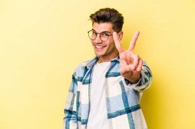 Sarı arka planda izole edilmiş genç beyaz adam neşeli ve kaygısız parmakları olan bir barış sembolü gösteriyor..