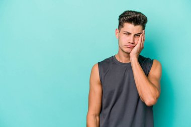 Mavi arka planda izole edilmiş, üzgün ve dalgın hisseden, kopyalama alanına bakan genç beyaz bir adam..