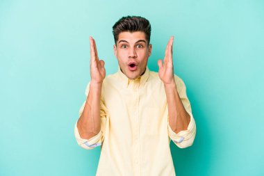 Kafkasyalı genç adam mavi arka planda izole edildi. Şaşırdı ve şok oldu..