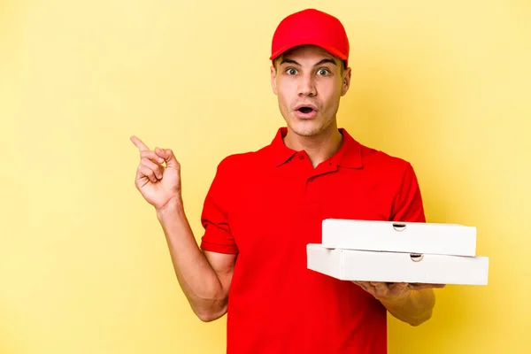 Young Delivery Caucasian Man Holding Pizzas Isolated Yellow Background Pointing — ストック写真