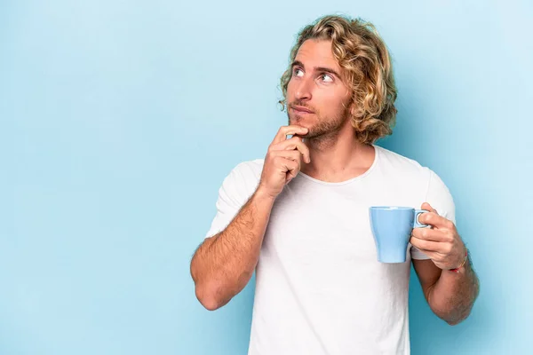 Young Man Holding Mug Isolated Blue Background Looking Sideways Doubtful — Fotografia de Stock