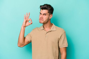 Kafkasyalı genç bir adam mavi arka planda izole edilmiş bir şekilde göz açıp kapayana kadar iyi bir el hareketi yapıyor..